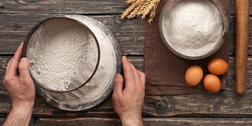 baker sift the flour on a dark rustic wooden background in a bakery. Top view with copy space