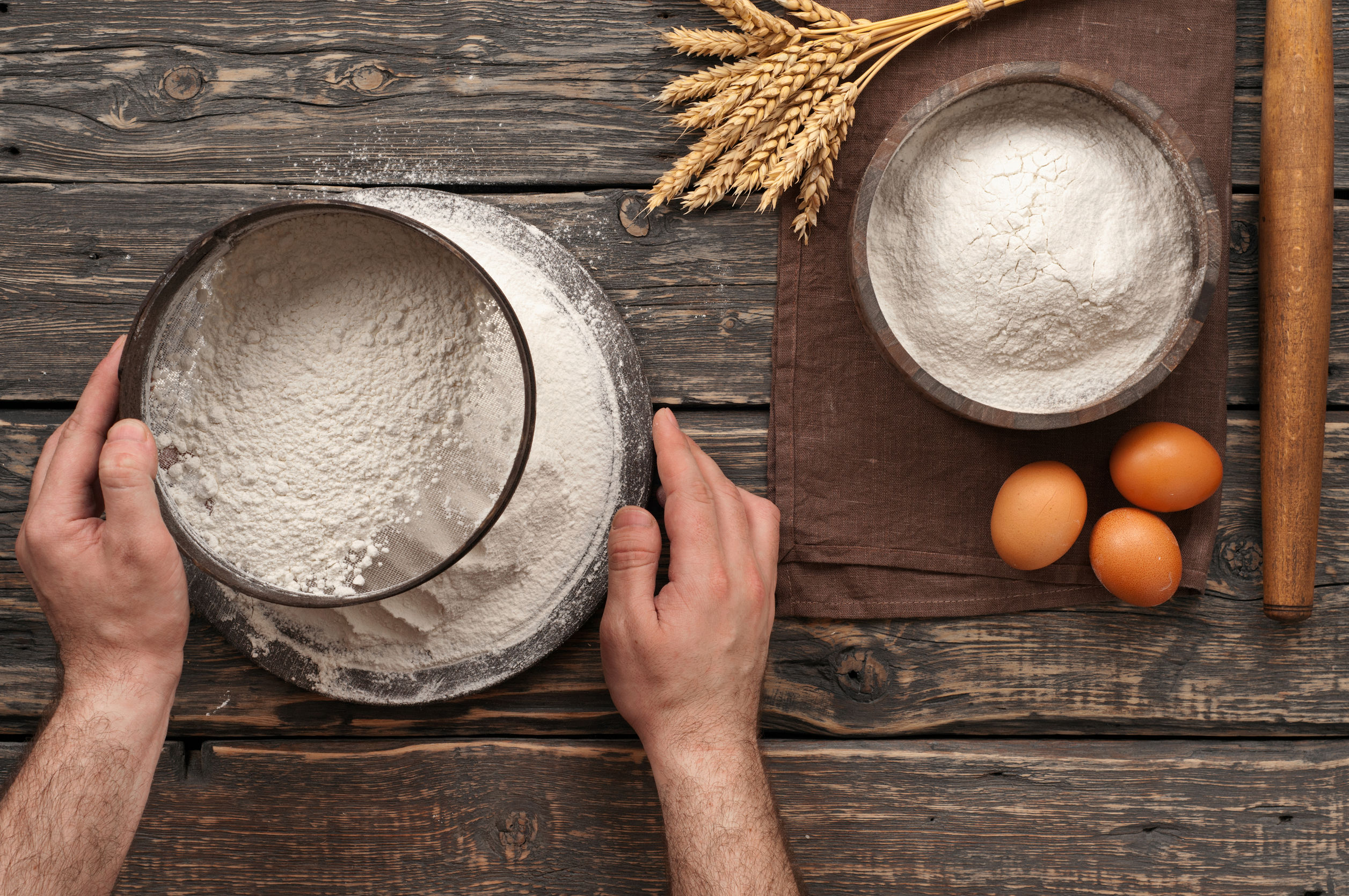 baker sift the flour on a dark rustic wooden background in a bakery. Top view with copy space